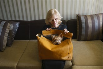 Woman holding on lap bag with Yorkshire terrier in living room