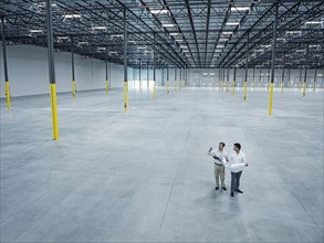 Architects with blueprint talking in empty warehouse
