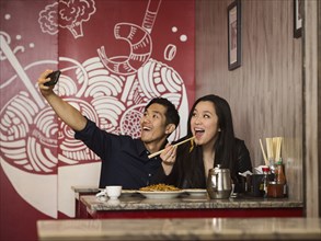 Chinese couple posing for cell phone selfie in restaurant