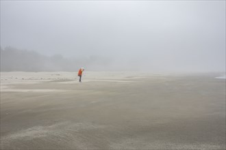 Woman in orange jacket standing on foggy beach