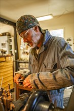 Senior artisan wood and metal craftsman works with tools in workshop