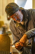 Senior artisan wood and metal craftsman works with power tools in workshop