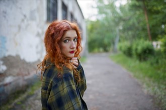 Redhaired woman posing next to old house