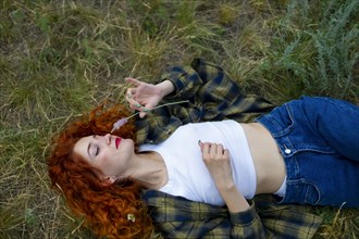 Redhaired woman lying on grass and smelling flower