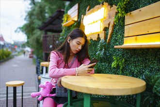 Young woman with smartphone sitting in sidewalk cafe