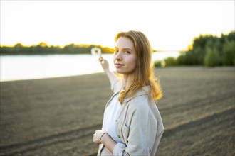 Portrait of woman holding flower on beach at sunset