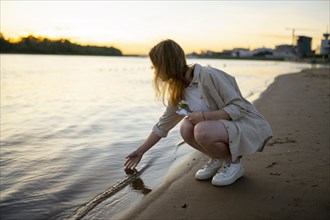 Woman touching water in river at sunset