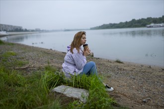 Thoughtful woman sitting on grass and looking at river