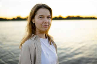 Portrait of thoughtful woman by river at sunset