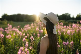 Young woman in straw hat standing in meadow on sunny day