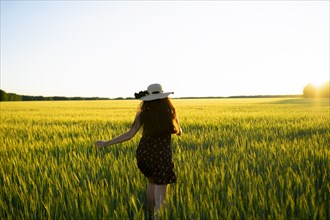 Rear view of woman in straw hat walking in field at sunset