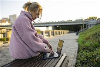 Woman working on laptop while sitting on bench at sunrise