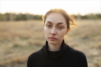Portrait of serious woman standing in field at sunset
