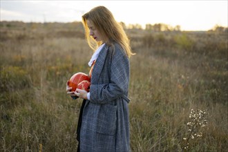 Side view of woman holding pumpkins in field
