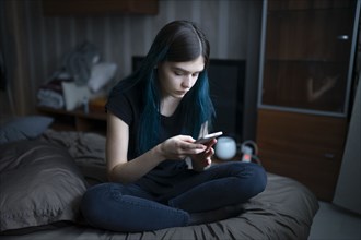 Serious woman using smart phone while sitting on bed