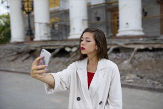 Portrait of young woman taking selfie with smart phone while standing in front of building