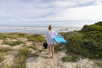 South Africa, Hermanus, Teenage girl walking on beach with body board
