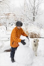 Boy with his dog building snowman