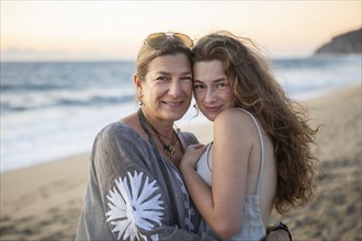 Portrait of smiling mother and teenage daughter on beach