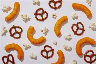 Overhead view of pretzels, cheese puffs and popcorn on white background