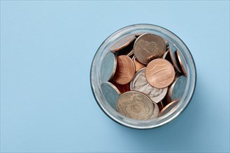 Overhead view of jar of coins on blue background