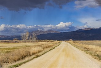 Empty dirt road leading to foothills under stormy skies
