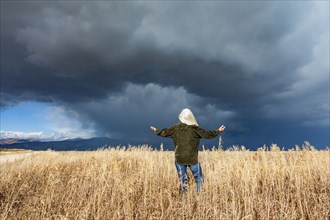 Rear view of woman standing in fall grasses under stormy sky