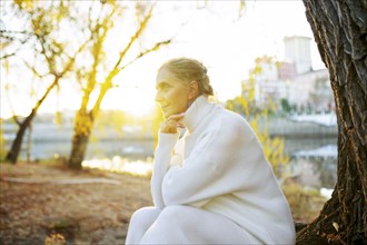 Woman in white sweater sitting by river in autumn