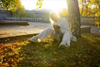 Woman with Yorkshire Terrier sitting on lawn in autumn