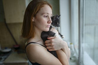 Pensive woman with cat looking through window