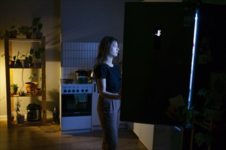 Woman standing in front of open refrigerator at night