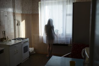 Rear view of woman looking through window in kitchen
