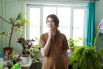Portrait of pensive woman surrounded with plants against window