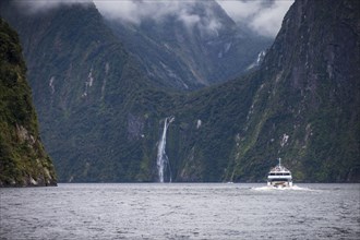 Ferry on fjord surrounded with mountains in Fiordland National Park