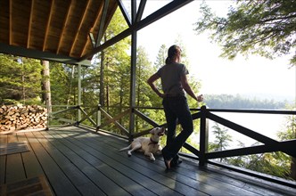 Woman with dog looking at lake from porch, Santa Clara, New York, USA