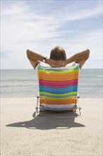 Rear view of man relaxing on deck chair on sandy beach, Nantucket, Massachusetts, USA