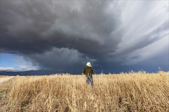 Rear view of woman standing in fall grasses under stormy sky, Fairfield, Idaho, USA