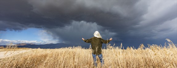 Rear view of woman standing in fall grasses under stormy sky, Fairfield, Idaho, USA