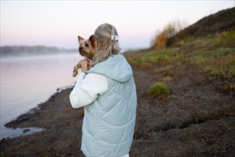 Rear view of woman holding Yorkshire Terrier on lakeshore, Omsk, , Russia