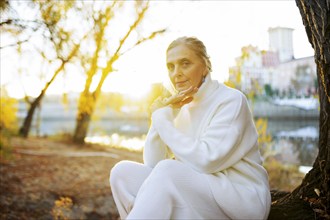 Portrait of woman in white sweater sitting by river in autumn, Omsk, , Russia