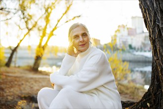 Portrait of woman in white sweater sitting by river in autumn, Omsk, , Russia