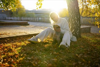 Woman with Yorkshire Terrier sitting on lawn in autumn, Omsk, , Russia