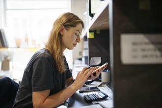 Woman looking at smart phone at desk in office, Omsk, , Russia