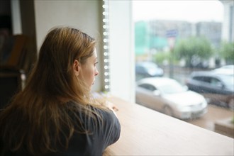 Woman leaning on window sill and looking through window, Omsk, , Russia