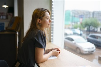 Woman leaning on window sill and looking through window, Omsk, , Russia