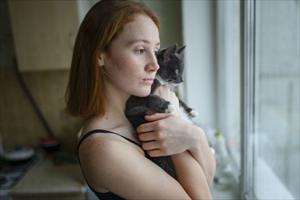 Pensive woman with cat looking through window, Omsk, , Russia