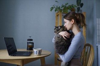 Woman holding cat and looking at laptop at home, Omsk, , Russia