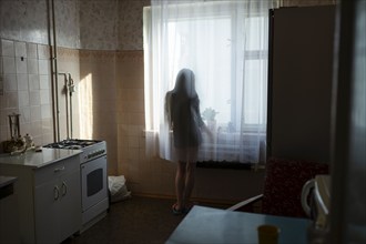 Rear view of woman looking through window in kitchen, Omsk, , Russia