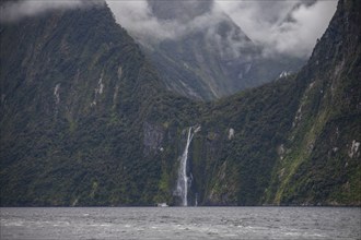 Ferry on fjord near waterfall in Fiordland National Park, Te Anau, Fiordland, New Zealand