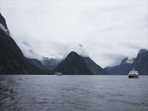 Ferries on fjord surrounded with mountains covered with clouds, Te Anau, Fiordland, New Zealand